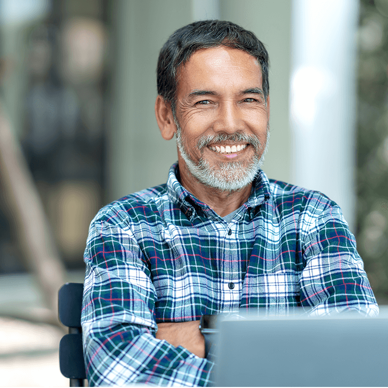 man smiling and crossing his arm in front of laptop